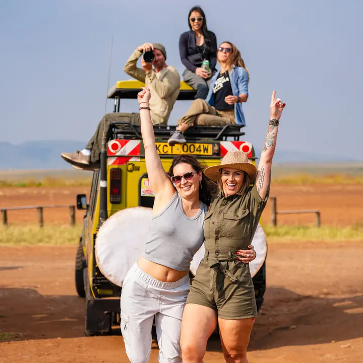 Two friends dancing in front of a safari jeep with the crew sitting on the roof in Kenya