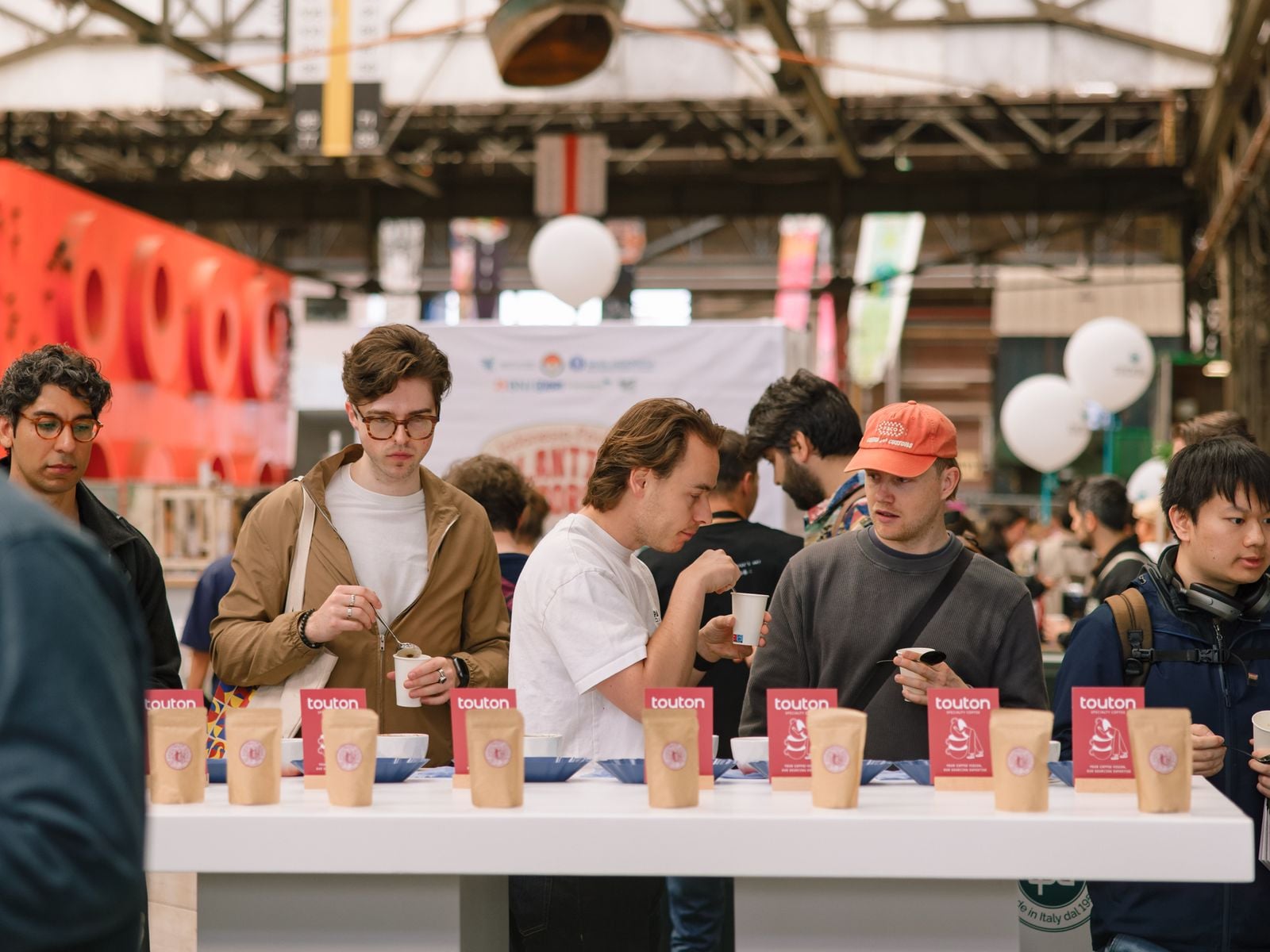 Visitors slurp coffee from spoons at a long open cupping table in the NDSM hall