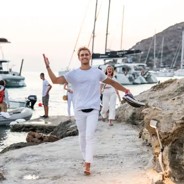 Walking up from the boats in all white with arms out on the SYB Greece trip