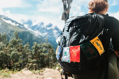 Prayer flags tied to a trekker's pack above Namche Bazaar with snow peaks behind