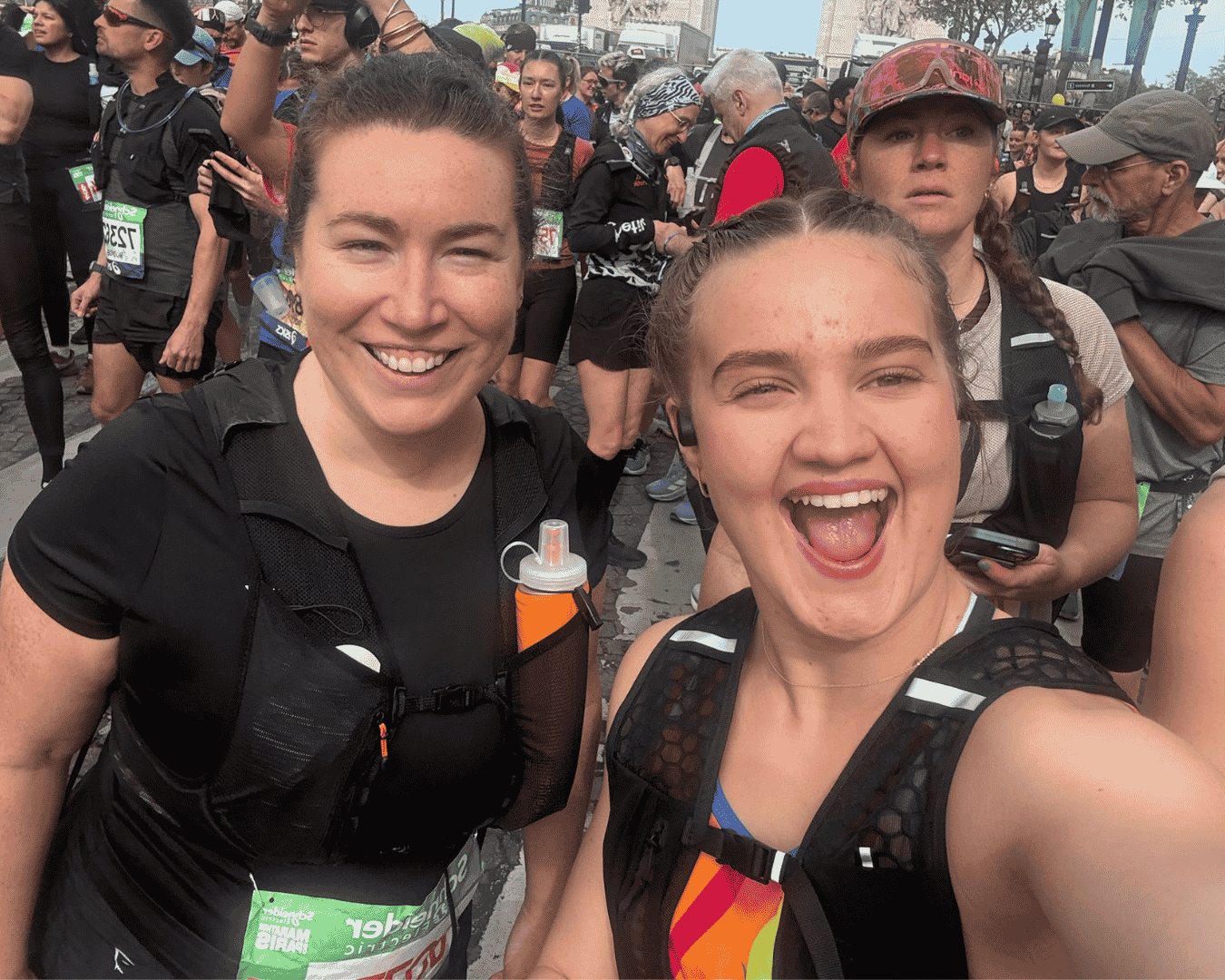 Two female runners in the Hardest Adventures Athens marathon cheering in a crowd of fellow runners.