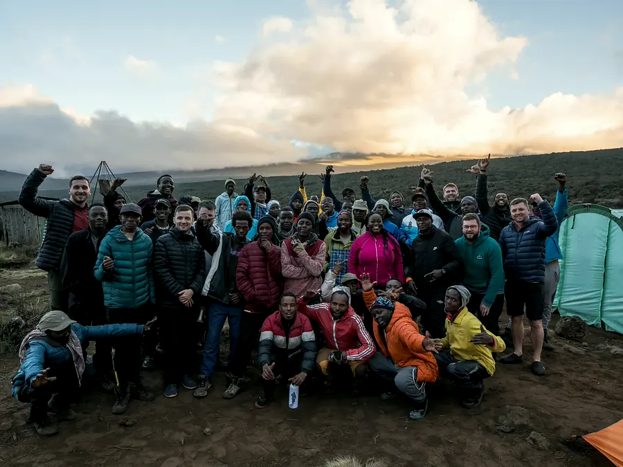 Full trek crew and climbers celebrating together at a Kilimanjaro camp at sunset