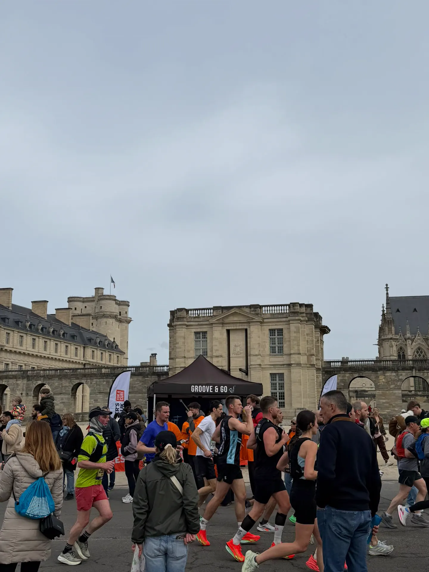 Crowd of runners passing the event village outside the Chateau de Vincennes on Paris Marathon race day.