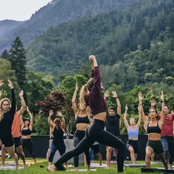 Group yoga class on the lawn with forested mountains behind on the SYB Dolomites trip