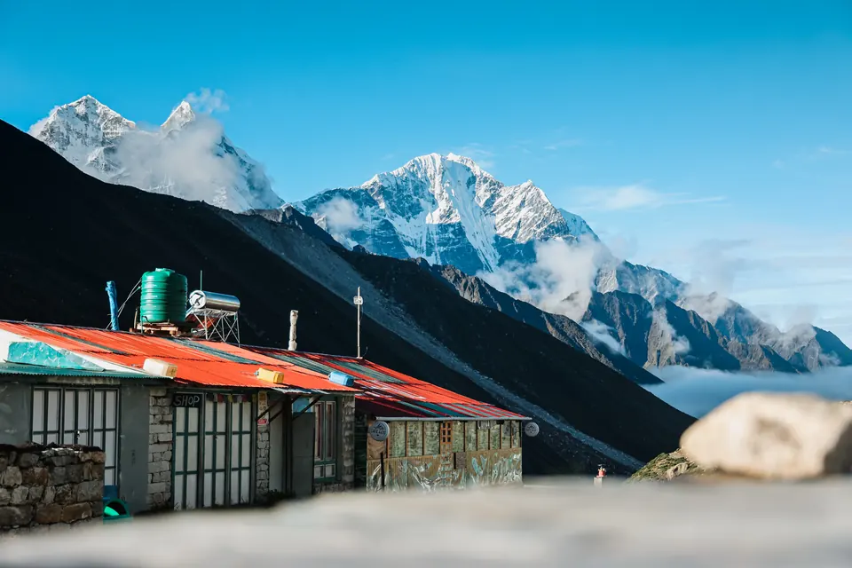 A high Khumbu teahouse with its water tanks, snow peaks rising above a sea of cloud behind