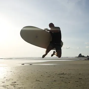 Jumping with a surfboard on the beach at sunset