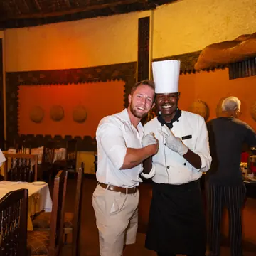 Guest posing with the chef in the lodge dining room on the SYB Kenya trip