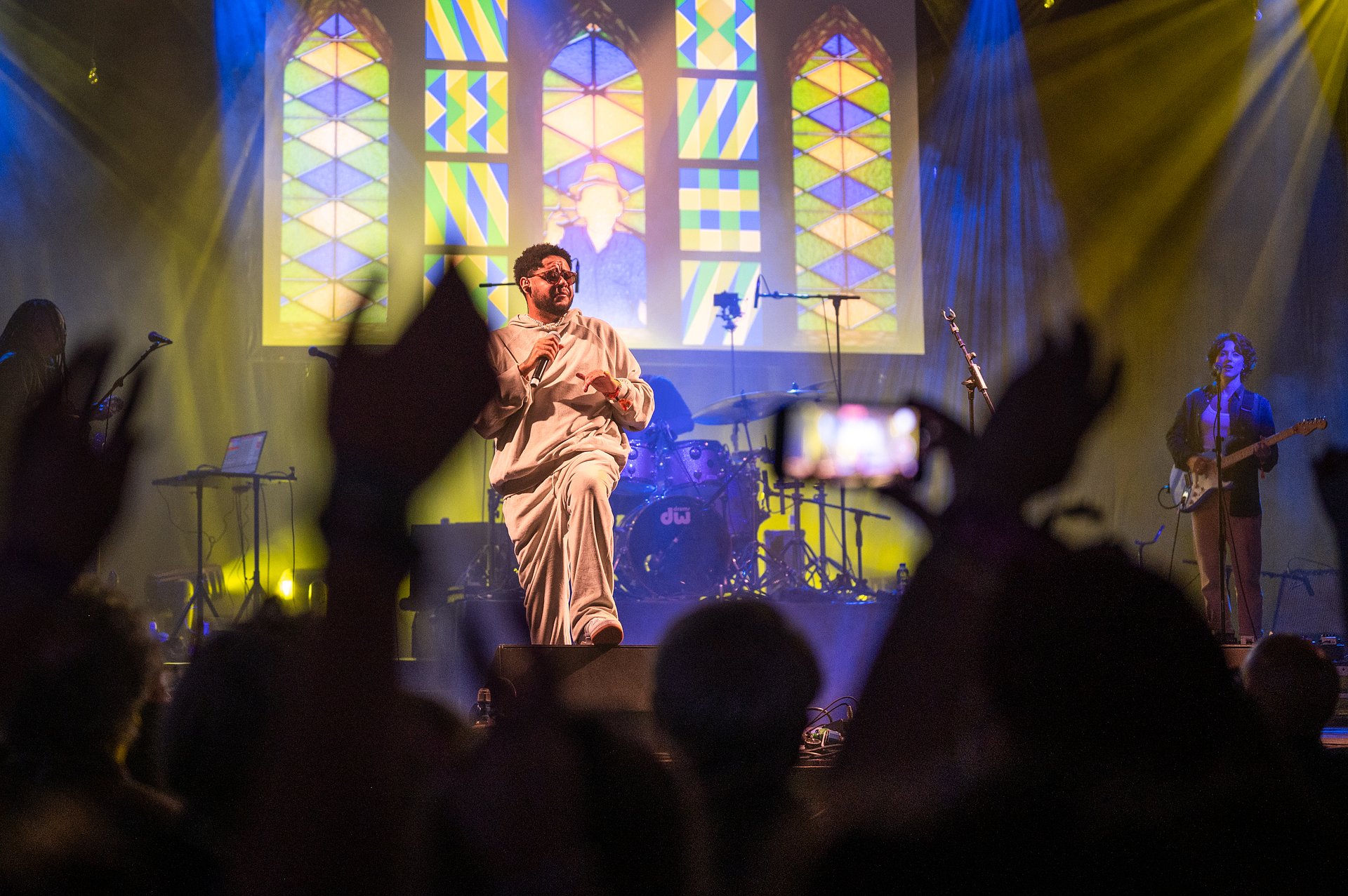 Brazilian rapper Emicida performing on stage. The crowd waves their hands in the air. 