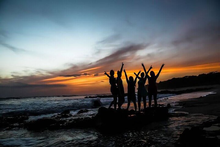 costa rica vacation packages girls with arms in air on rock beach at sunset