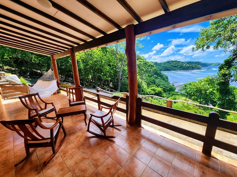A covered terrace with wooden chairs looking over the bay at Villas Playa Maderas