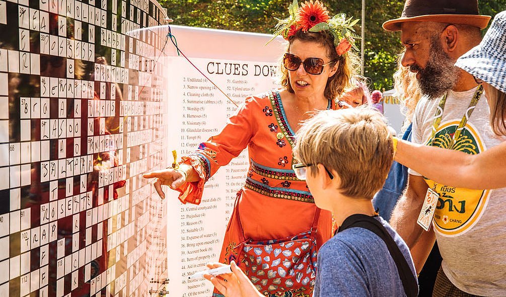 A man, woman and child playing a giant crossword, drawing letters onto the board with a whiteboard pen. 
