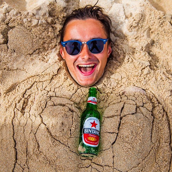 Kuta Bali Indonesia_male traveller buried in the sand with local bintang beer