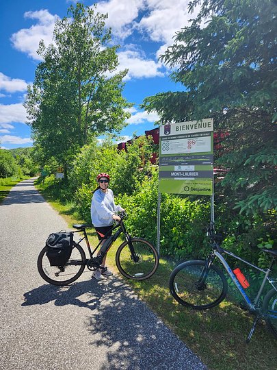 Woman standing with her bike next to a sign indicating the start of P'tit Train du Nord trail in Mont Laurier Quebec