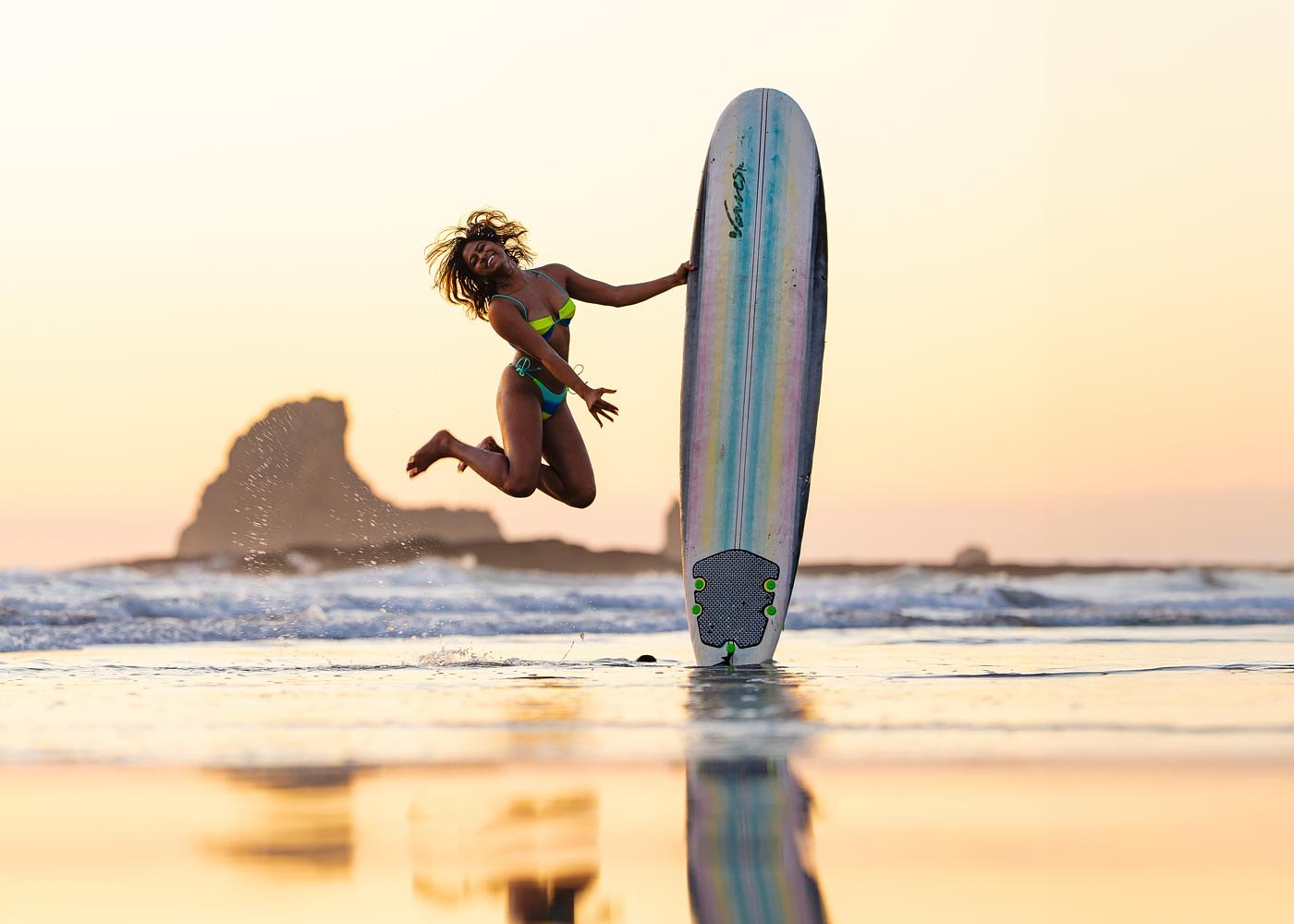Surfer jumping with her board at sunset, Playa Maderas, Nicaragua