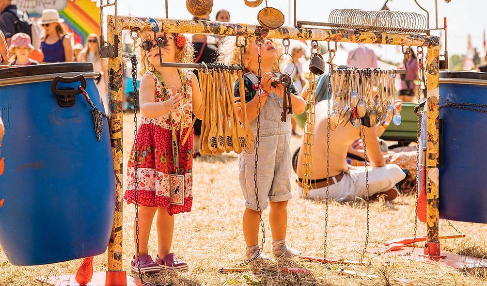 Two toddlers playing with instruments made from oil barrels and wooden spoons