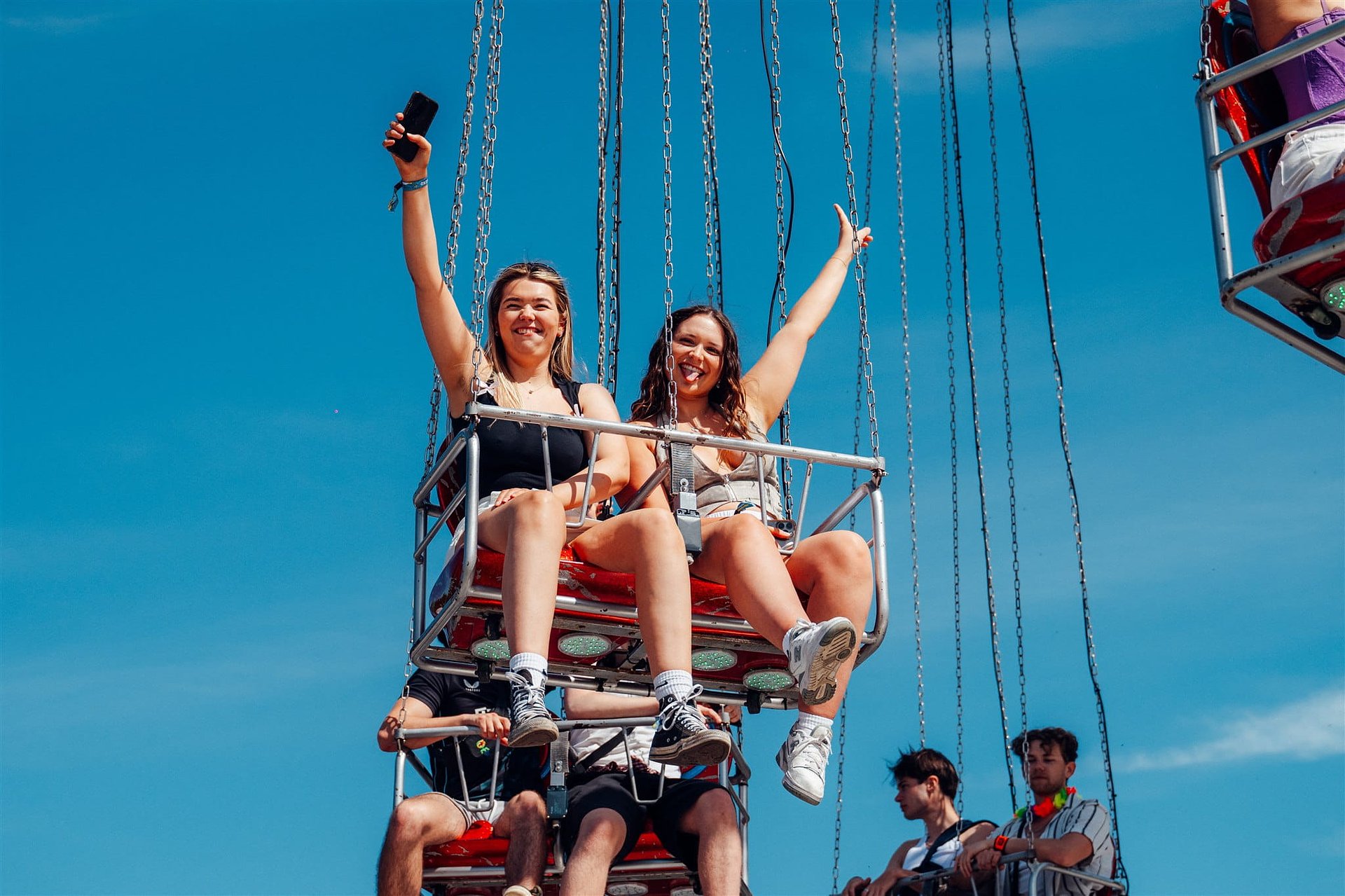 Two girls raise their arms as they enjoy the funfair ride at Bournemouth 7s Festival in Dorset