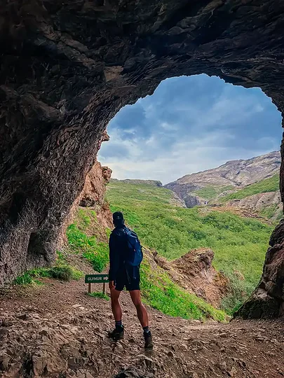 A hiker on a cliff path above a green Icelandic canyon