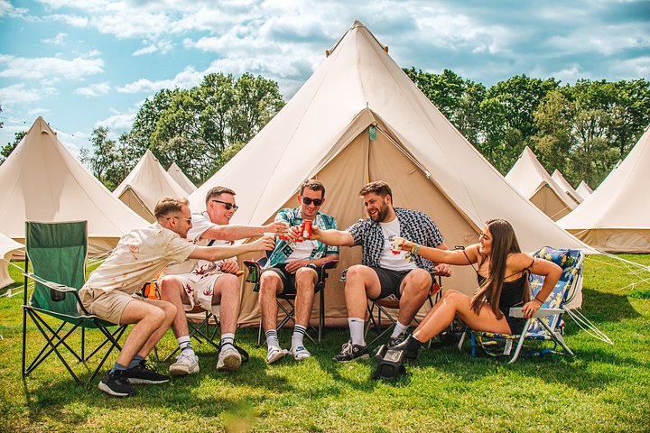 Group of friends sat outside a glamping bell tent having a drink in the glampsite at Bournemouth 7s Festival, in Dorset England.