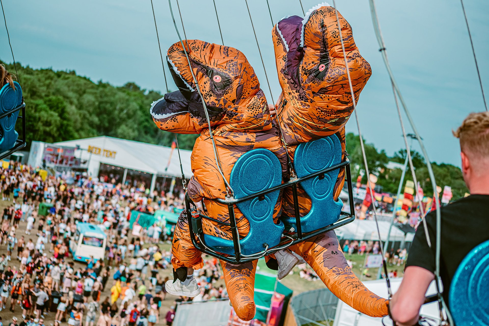 Two people in Dinosaur inflatable fancy dress costumes ride the funfair swing in the air overlooking the main festival arena at Bournemouth 7s Festival, in Dorset