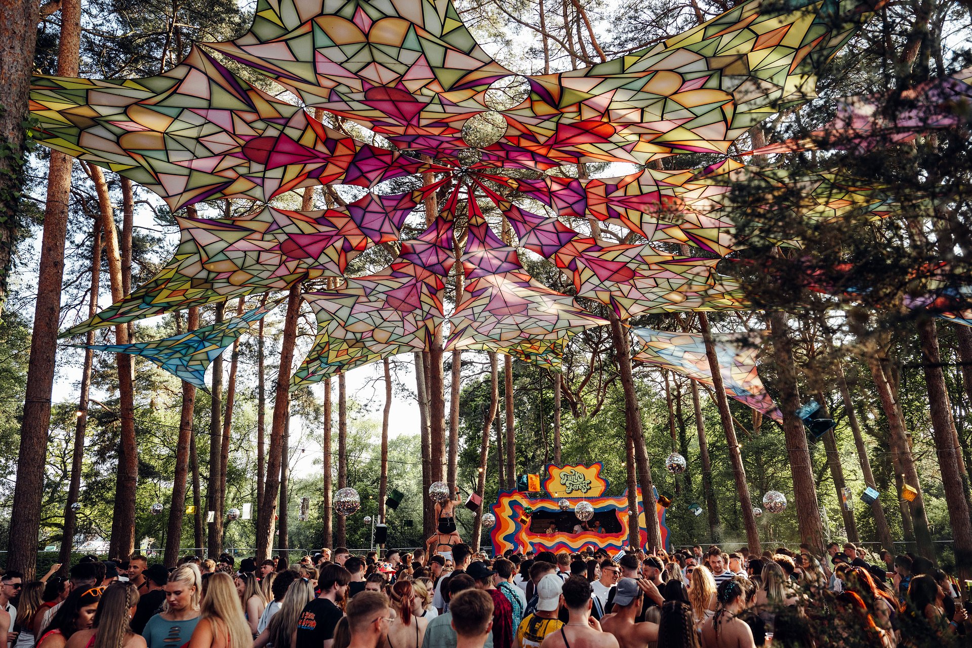 Funky Forest music stage arena, with a large crowd deep within the woodland forest playing funky house and disco, at Bournemouth 7s Festival, in Dorset.