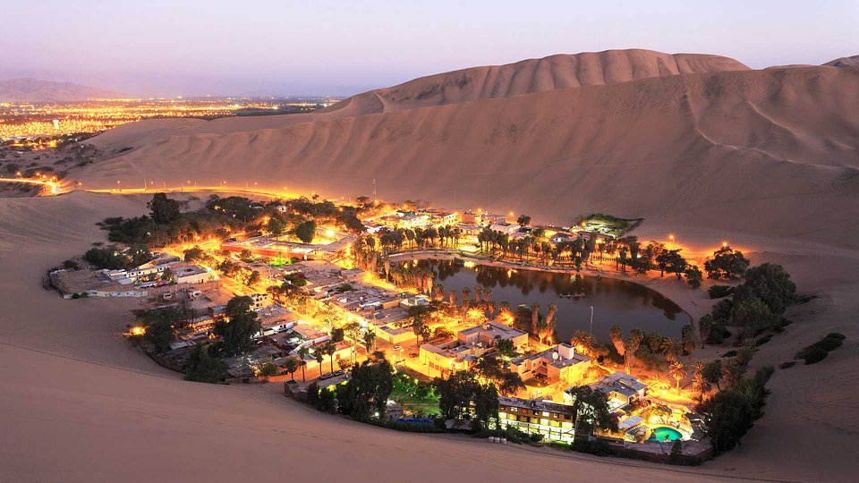 The Huacachina oasis lit up at dusk among the dunes