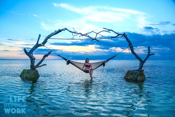 girl sitting on a hammock suspended over water in bali during sunset best things to do in bali