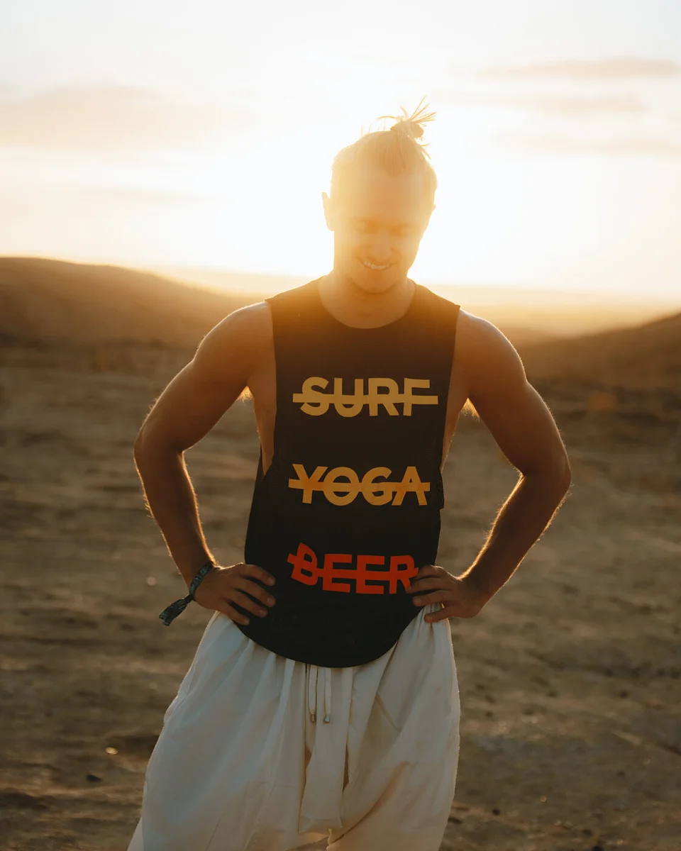 A traveler in a Surf Yoga Beer tank top with the sun setting behind him in the desert