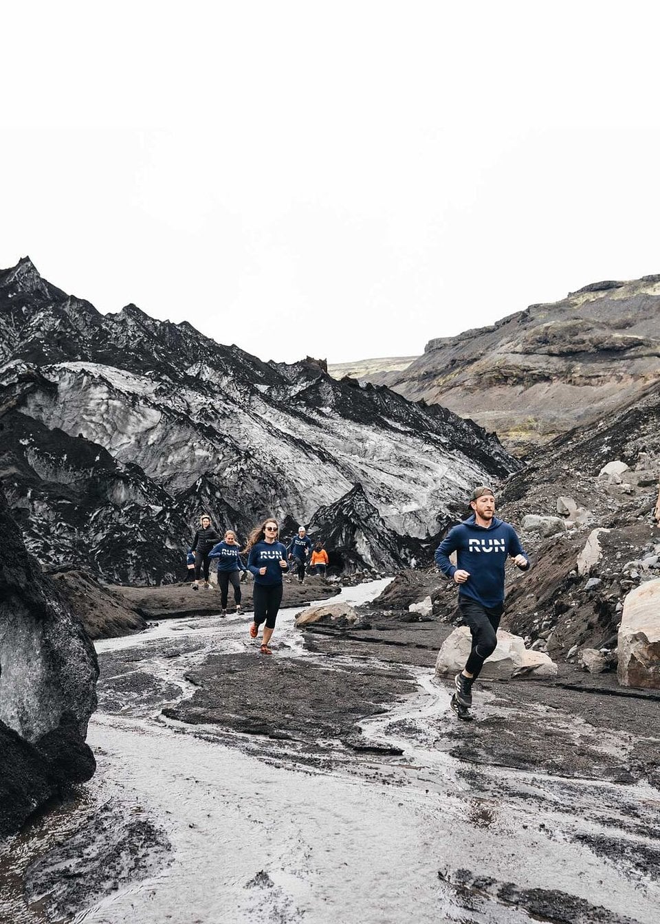 Trail runners on a dark ash trail below a glacier in Iceland