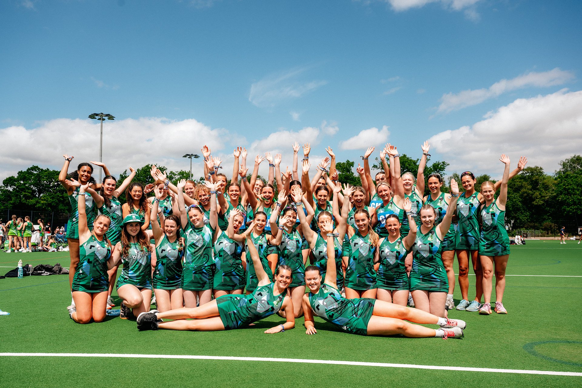 Large group of netball girls pose with their hands in the air on the court, at Bournemouth 7s Festival.