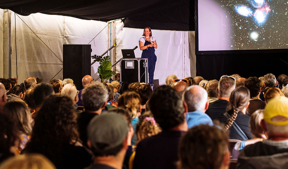 A woman giving a talk to a crowd in the physics tent