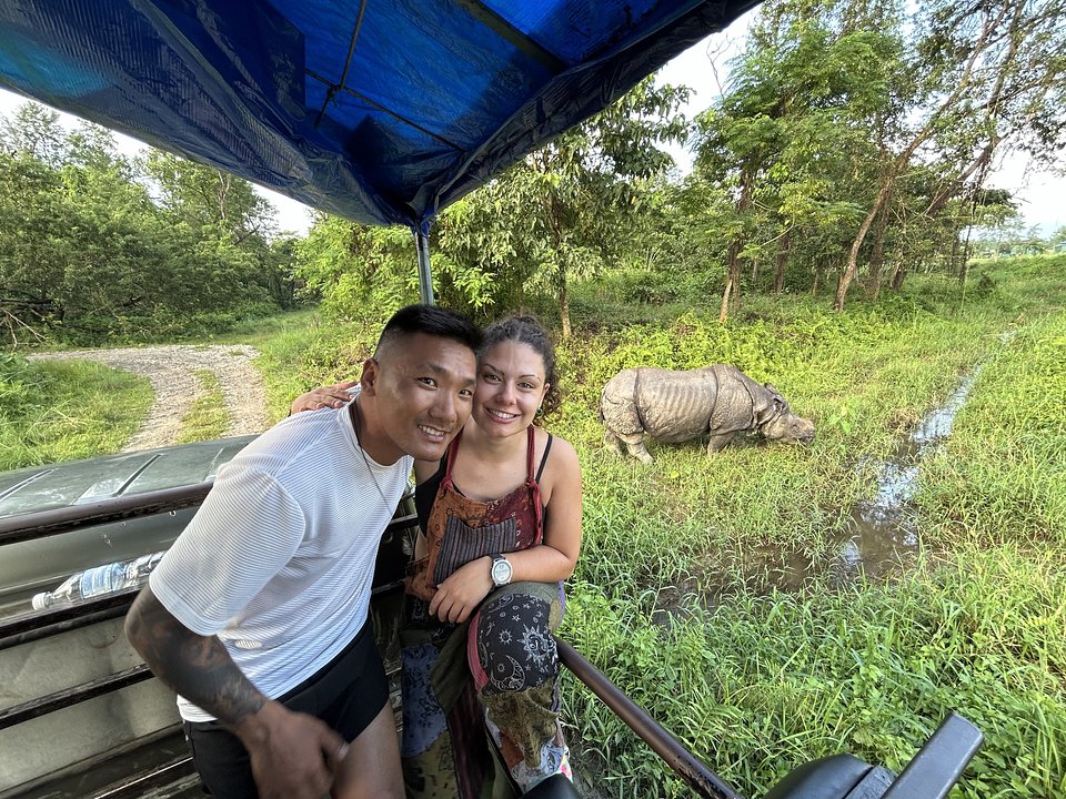 Two travellers on a Chitwan jeep safari, a one-horned rhino behind them
