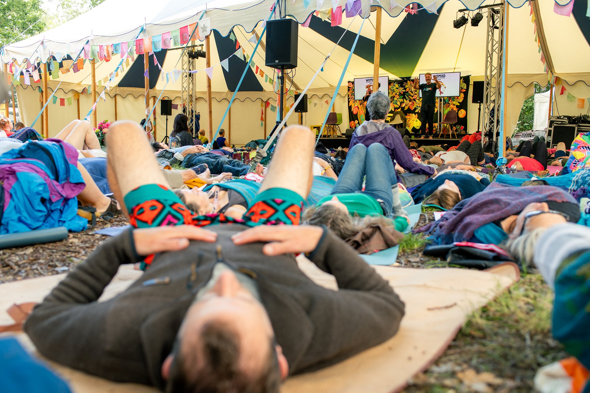 A breathwork workshop at the world of words stage. The audience are lying on mats on the floor. 